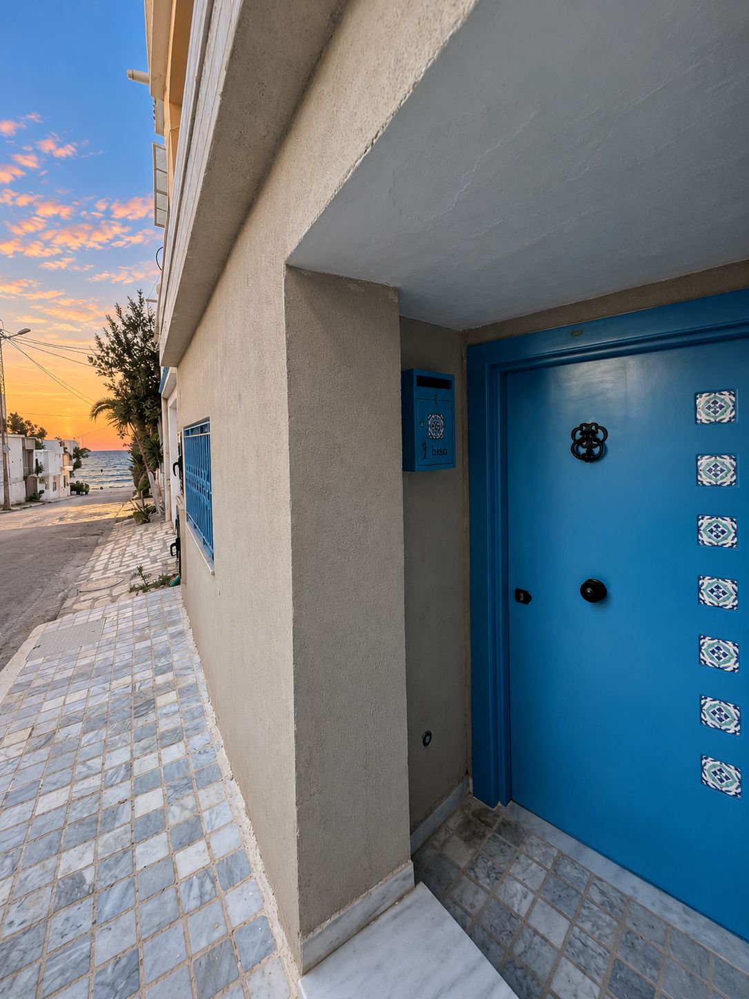 Un edificio con puerta azul, buzón y acera de baldosas.