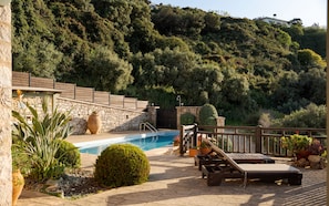 A pool area with a stone wall, lounge chairs, and a view of a hillside. - VILLA THEA, Your Villa (Chania)