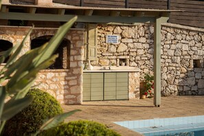 Um edifício de pedra com piscina, aviso proibindo mergulhos e área coberta com pia.