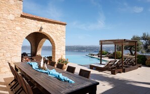 A stone building with an archway, a wooden table with chairs, a pool area with lounge chairs, and a pergola. - VILLA ONIRO, Your Villa (Chania)