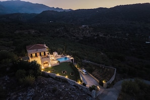 Una villa con piscina, rodeada por un muro de piedra, ubicada en un paisaje montañoso.