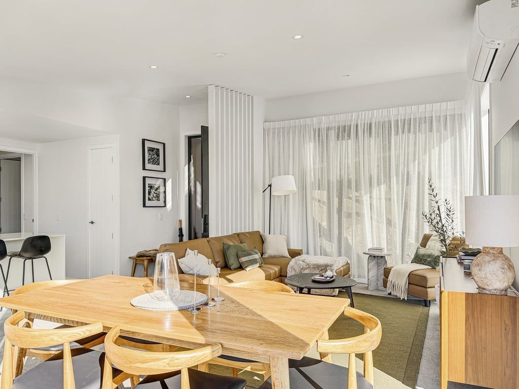 A modern living room with a dining area, featuring a wooden dining table, chairs, a sofa, and a coffee table.