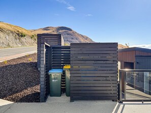 Une zone délimitée par une clôture en métal, avec une poubelle et un bâtiment en arrière-plan.