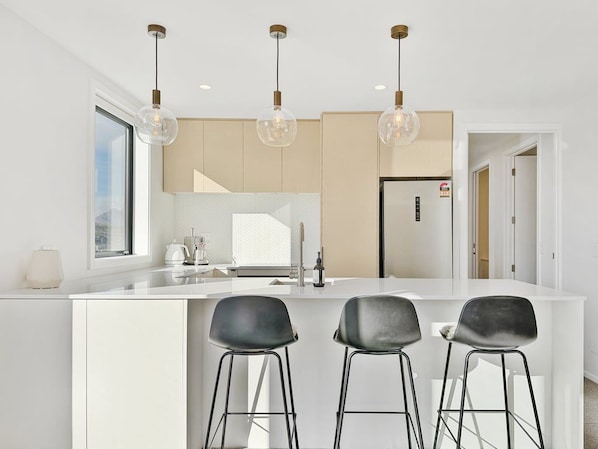 Une cuisine moderne dotée d’un îlot central, de trois tabourets de bar, d’un éclairage suspendu et d’un réfrigérateur.