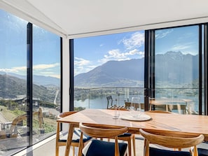 A dining area with a table and chairs, large windows with a mountain view, and a glass railing.