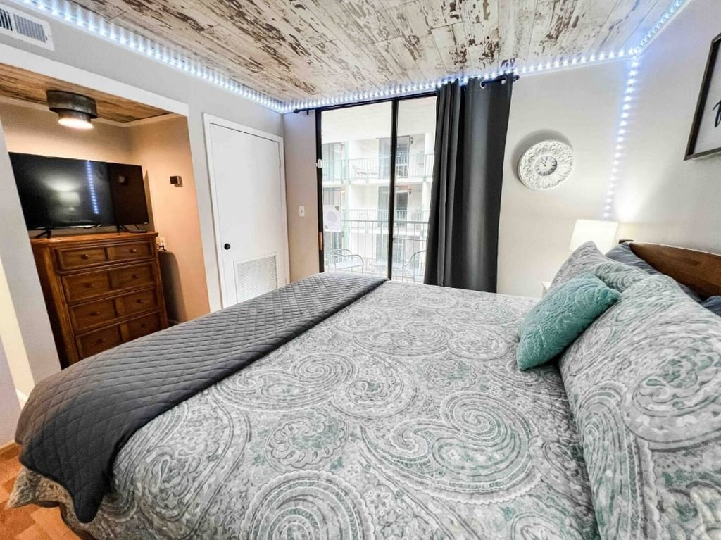 Een slaapkamer met een bed, een televisie, een dressoir en een balkon met uitzicht.