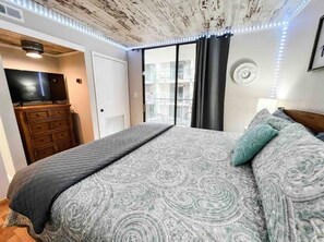 Een slaapkamer met een bed, een televisie, een dressoir en een balkon met uitzicht.