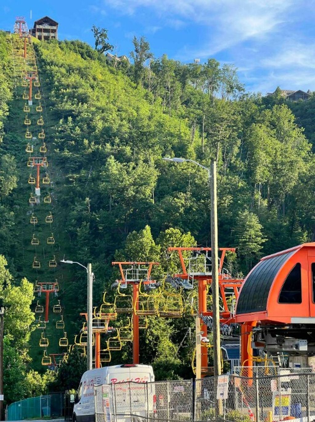 Eine Seilbahn mit Sesseln, die an Seilen befestigt sind, umgeben von dichtem Wald und wolkenlosem Himmel.