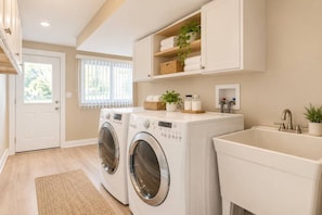 A laundry area with two front-loading washing machines, a sink, and a window with blinds. - Spacious 5BR Arlington Heights Retreat (Arlington Heights)