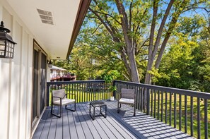 A wooden deck with two chairs and a table, overlooking a backyard with trees and a house. - Spacious house Rockford (Rockford)