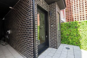 Ein modernes Gebäude mit Backsteinfassade, einem Glastür-Eingang und einem kleinen Garten mit Grünpflanzen.