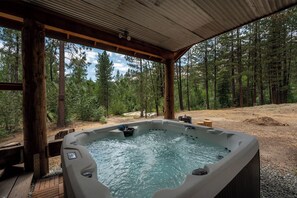 Een hottub in een bebost gebied met een houten terras en een metalen dak.