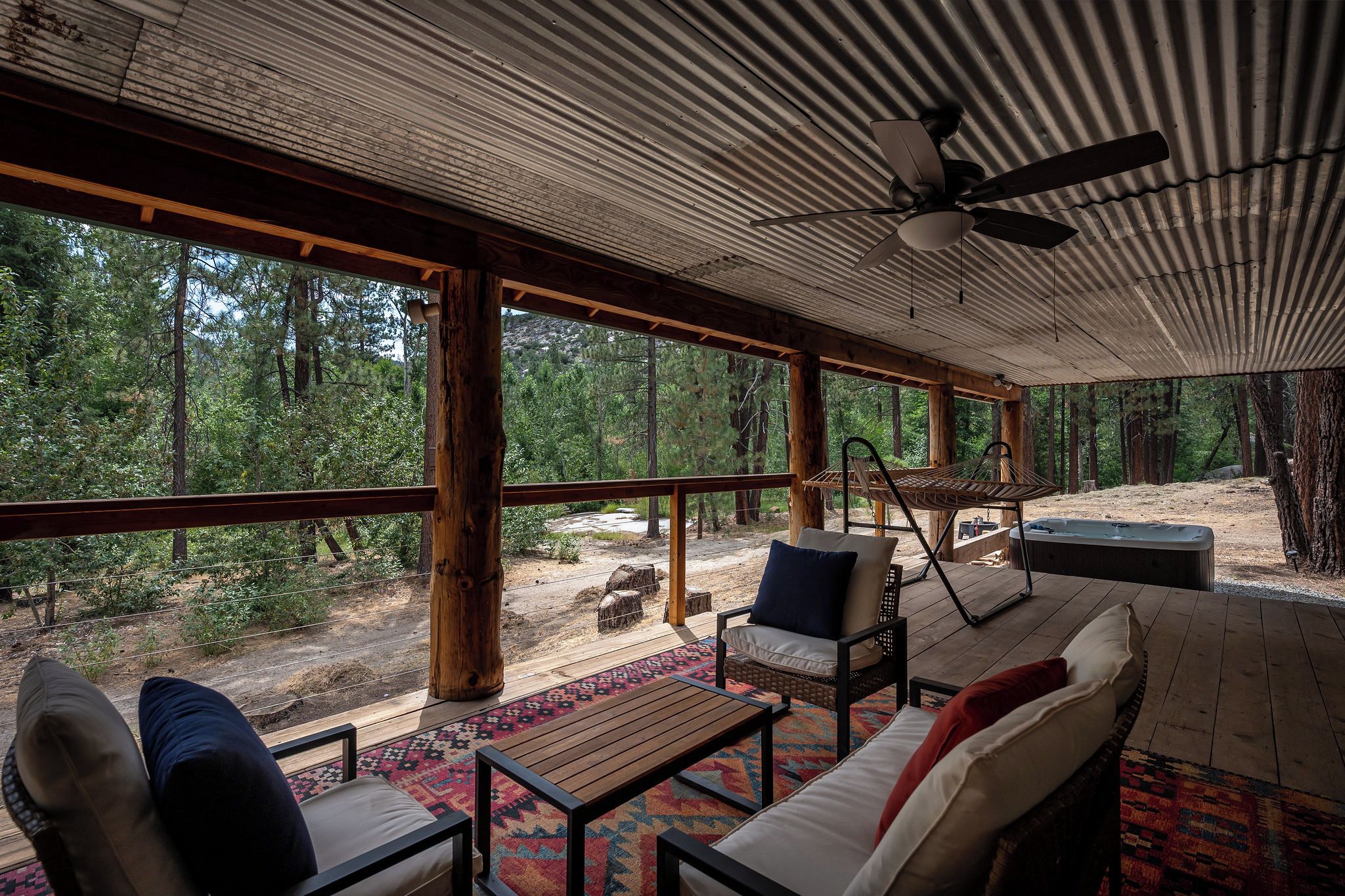Un espacio de estar al aire libre cubierto con vistas a un bosque, un ventilador de techo y un jacuzzi.