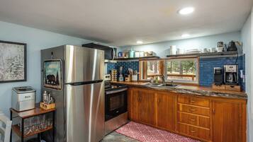 Una cocina compacta con un refrigerador de acero inoxidable, un horno empotrado y un microondas. Hay una encimera de madera con un lavamanos y una ventana arriba.