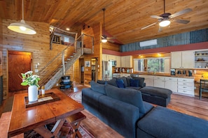 A spacious living area with a wooden staircase, a sofa set, a dining table, and a kitchen area.