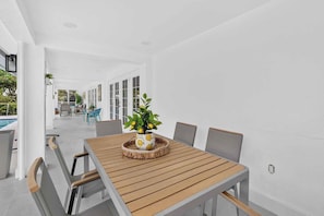Un espace repas moderne avec une table et des chaises en bois, une plante en pot et une vue sur une piscine et un coin salon extérieur.