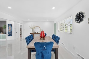 Un espace repas comprenant une table en marbre, des chaises à revêtement bleu, un vase rouge servant de centre de table et une décoration florale fixée au mur.