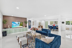 Un salon moderne avec un téléviseur à écran plat, des canapés bleus, une table basse et, au fond, un coin repas.