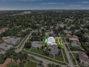 An aerial view of a residential area with a large house featuring a swimming pool, surrounded by smaller houses and greenery. - McGregor Oasis: 4BR/ 5BTH Private Pool & Game Room (Fort Myers)