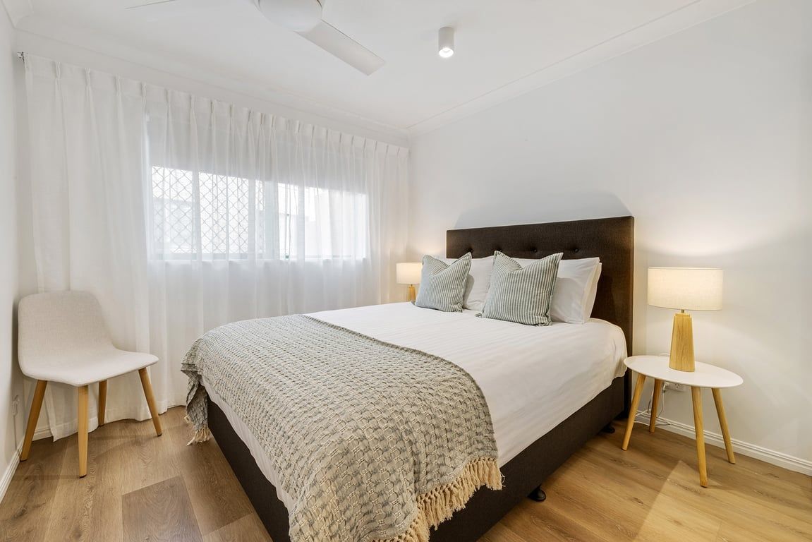A bedroom with a bed, two bedside tables, a chair, and a window with curtains.