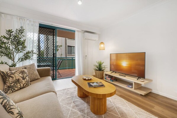 A modern living room with a sofa, a coffee table, a TV, and a balcony with a view.