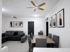 A modern living room with a sectional sofa, a dining table with chairs, a ceiling fan, and framed artwork on the walls. - Nice Apt+Pool+Beach Club+Parking+Gym+AC@Acapulco Diamante (Acapulco)