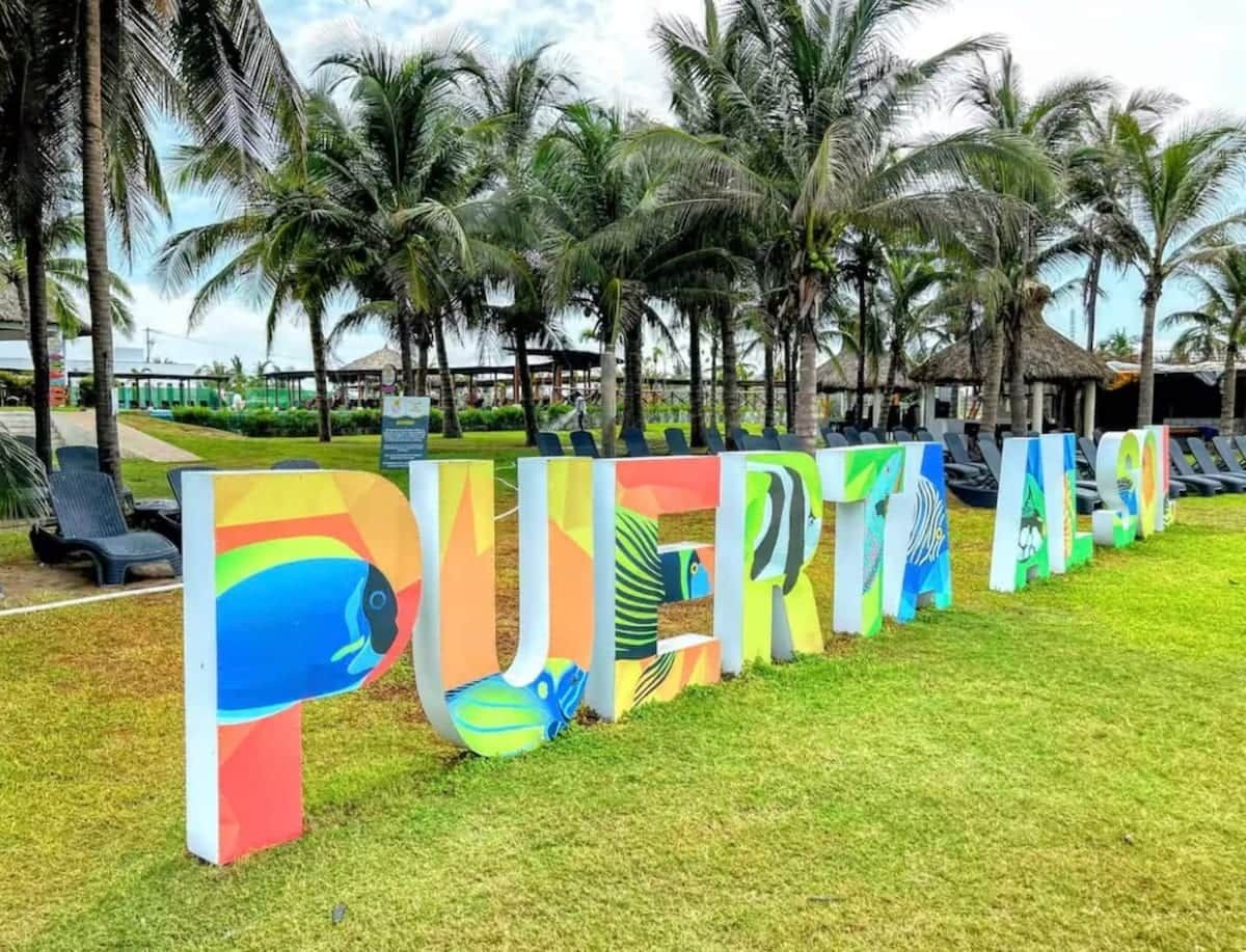 A sign with colorful letters spelling 'PUERTO RICO' in a grassy area with palm trees.