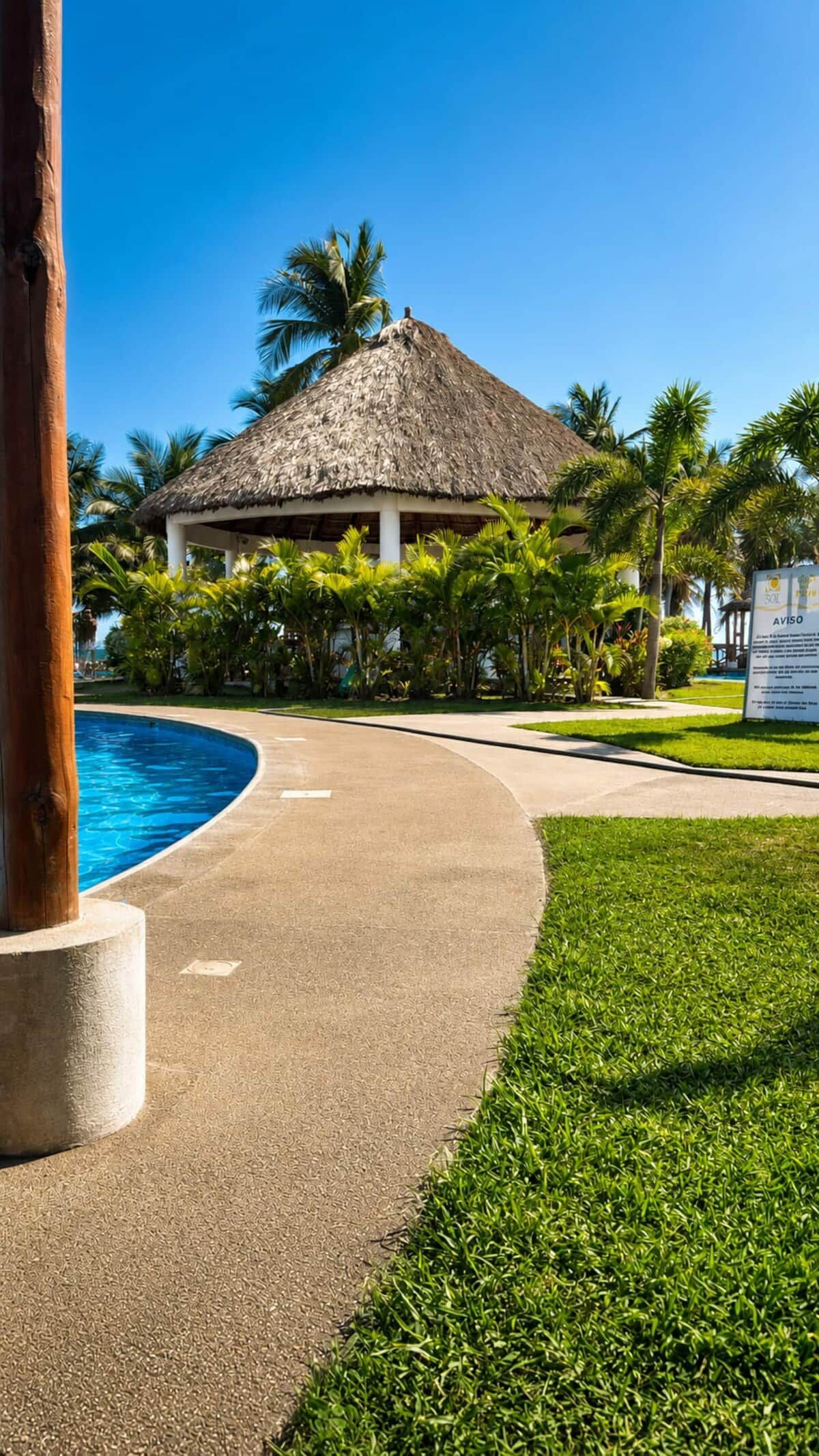 A resort with a thatched-roof structure, a swimming pool, and lush greenery.