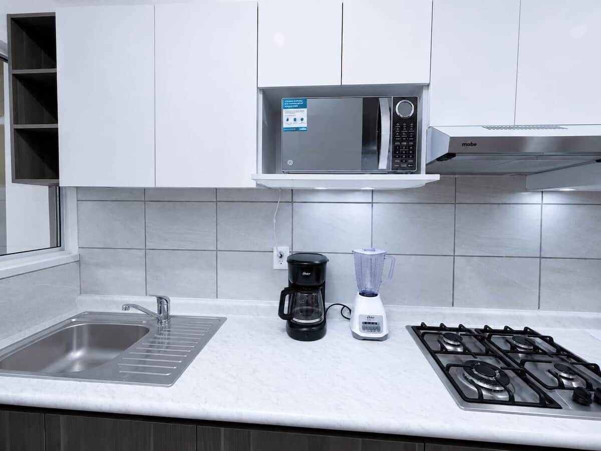 A kitchen with a stainless steel sink, a coffee maker, a blender, and a gas stove.