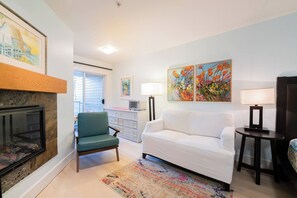 Una sala de estar con chimenea, un sillón verde, un sofá blanco, un tapete colorido y obras de arte en las paredes.