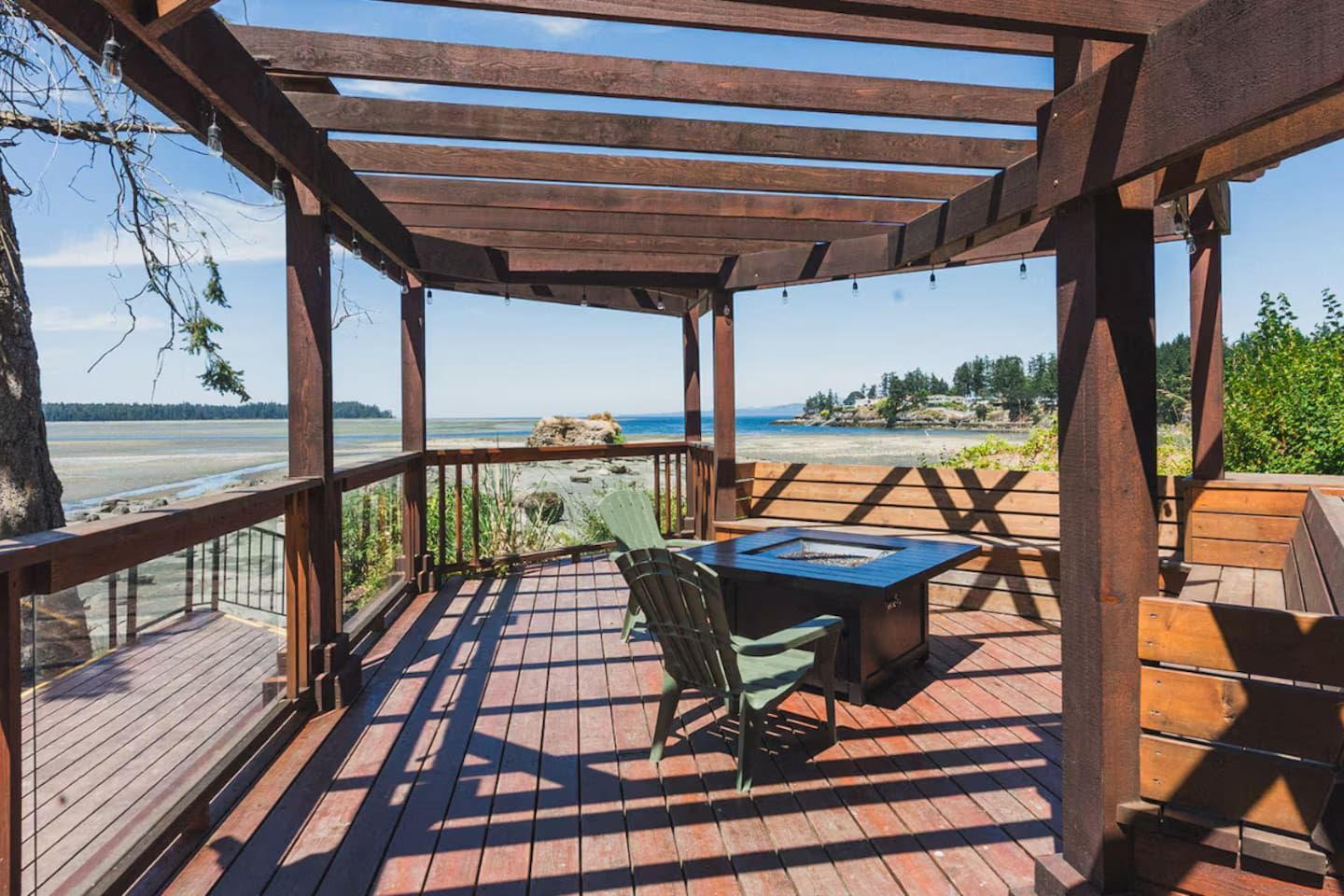 Une terrasse en bois avec une pergola, une table et une chaise, donnant sur une plage.