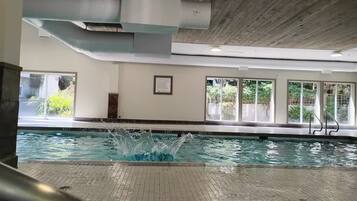 Una piscina interior con agua cristalina, piso de baldosas y un letrero que indica 'no saltos'.
