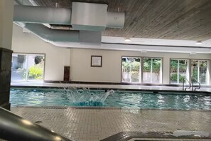 Una piscina interior con agua cristalina, piso de baldosas y un letrero que indica 'no saltos'.