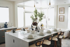 A modern kitchen with a large island, white cabinetry, and a dining area with a white table set for six. - North Beacon Hill Seattle Retreat, Sauna, Jacuzzi Tub, King Bed, Central Locale! (Seattle)