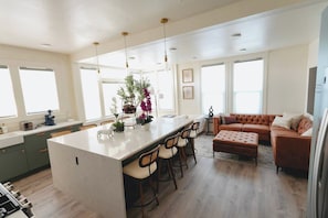 Cocina moderna con una isla central, taburetes de bar y una zona de estar con sofá de cuero.
