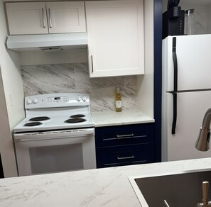 Uma cozinha compacta com fogão branco, uma garrafa de vinho no balcão e uma geladeira.