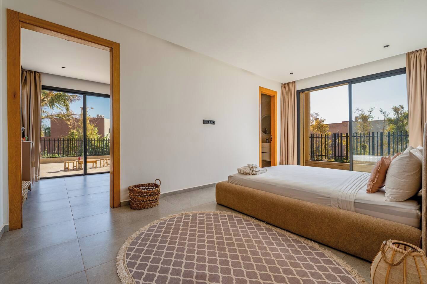 A modern bedroom with a large bed, a small round rug, and a view of the outdoors through a sliding door.