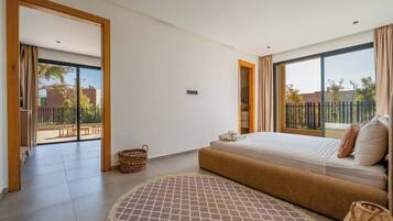 A modern bedroom with a large bed, a small round rug, and a view of the outdoors through a sliding door.