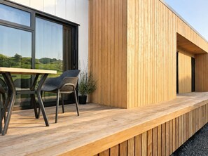 Een modern buitseizoen met een houten terras, een tafel en twee stoelen.