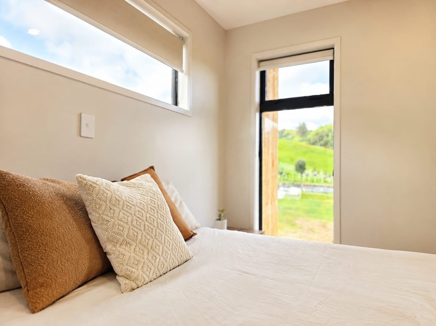Ein Schlafzimmer mit einem Bett, Kissen, einem Fenster und Blick ins Grüne.