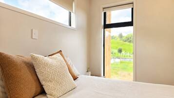 Ein Schlafzimmer mit einem Bett, Kissen, einem Fenster und Blick ins Grüne.