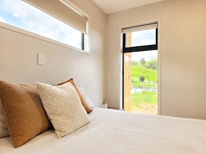 Un dormitorio con cama, almohadas, una ventana y vistas a zonas verdes.