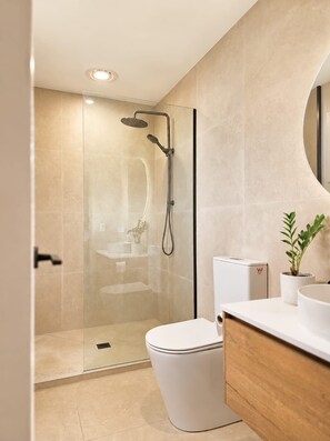 Een moderne badkamer met een douchecabine van glas, een wit toilet en een houten wastafelmeubel.