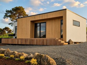 Een modern gebouw met een houten gevel, grote ramen en een grindpad.