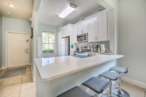 A modern kitchen with white cabinetry, a stainless steel refrigerator, a microwave, and a large island with bar stools. - Spacious Resort Home with 2 Master Bedrooms - Near Disney & Universal Studios (Davenport)