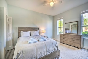 Une chambre à coucher comprenant un lit, une commode, un miroir, un ventilateur de plafond et une fenêtre.