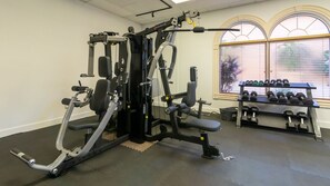 Une salle de sport équipée de matériel d’exercice, une fenêtre avec des stores et un porte-haltères.