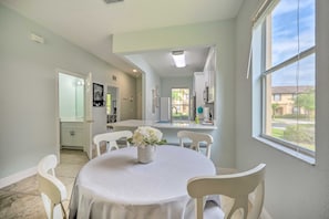 A dining area with a round table, white chairs, and a vase of flowers. There is a kitchen visible in the background with white cabinets and a window. - Spacious Resort Home with 2 Master Bedrooms - Near Disney & Universal Studios (Davenport)