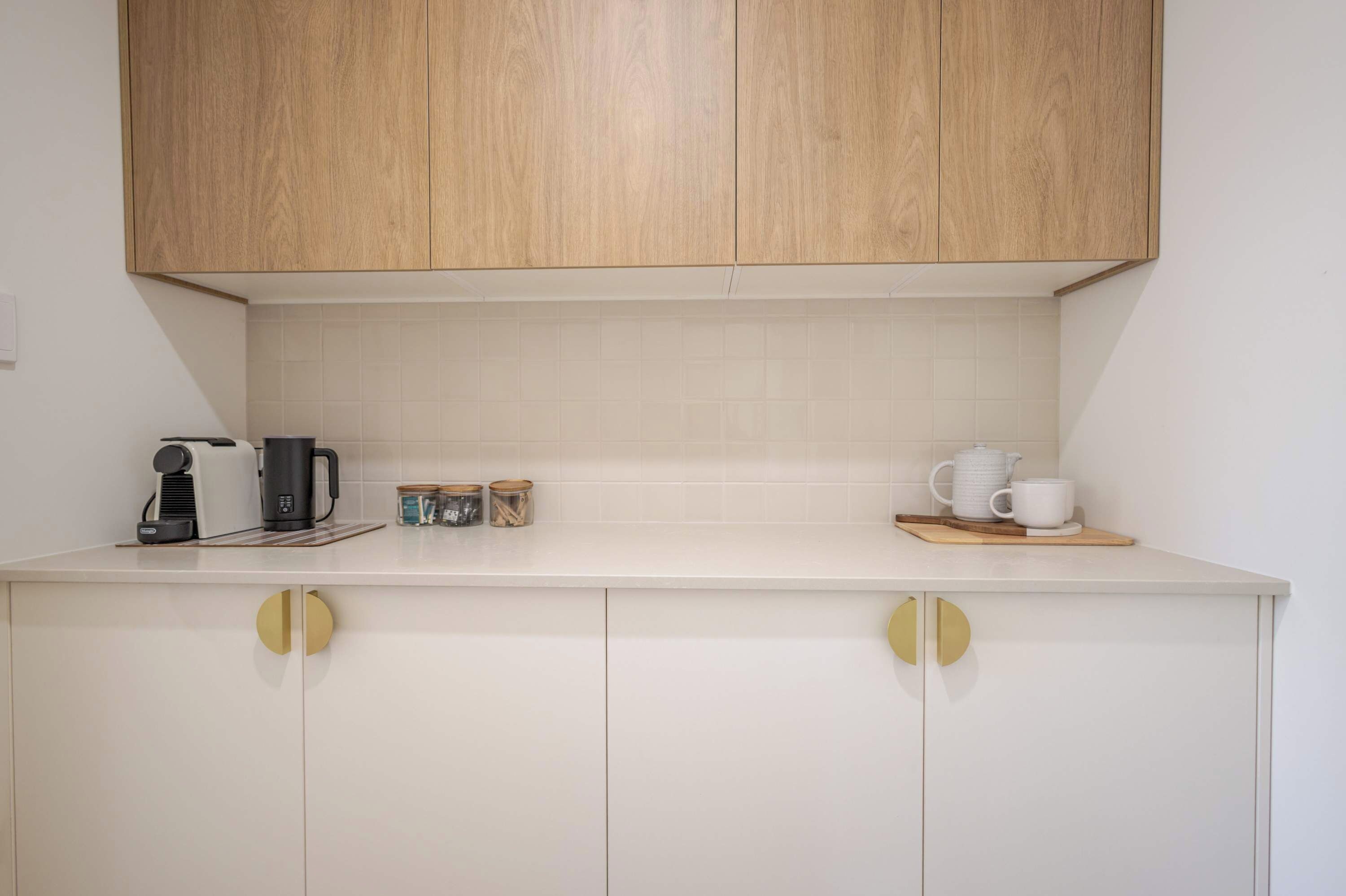 A kitchen with wooden cabinets, a coffee maker, jars, and a kettle on the counter.