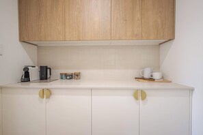 Una cocina con alacenas de madera, cafetera, frascos y tetera sobre la encimera.